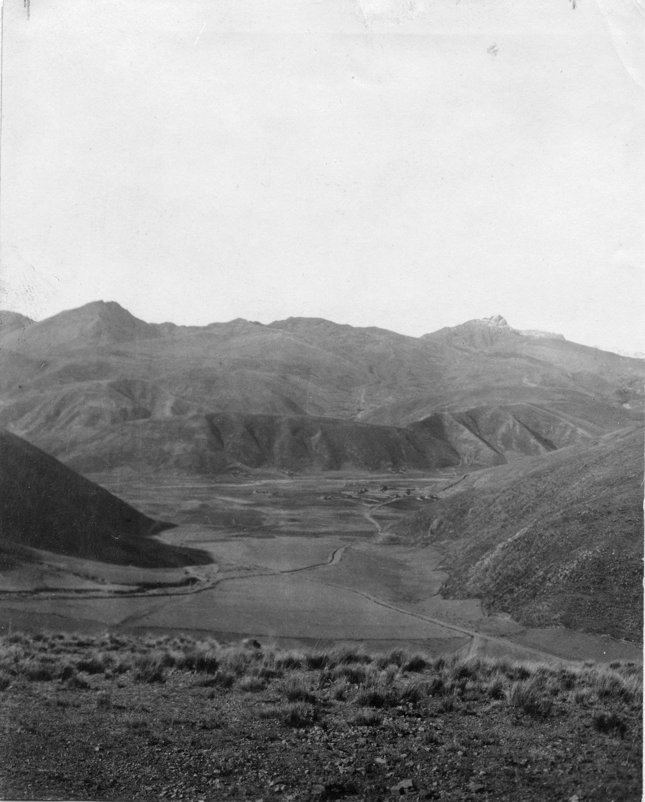 Fotografía en blanco y negro de un valle andino árido con laderas peladas y cerros superpuestos que se pierden en la distancia.